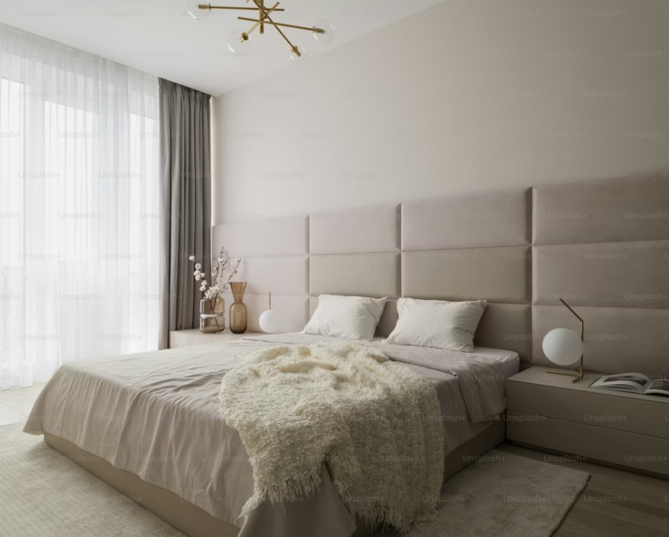 Well-dressed bed in a bright modern bedroom with upholstered headboard and neutral furnishings.