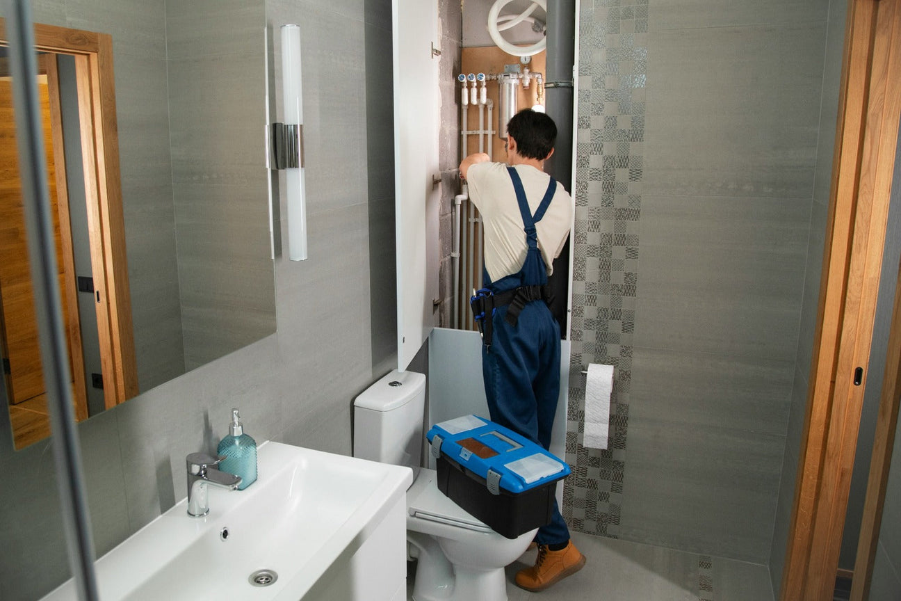 Professional plumber working in a modern bathroom with plumbing and heating fixtures.