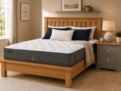 Oak wooden bed frame styled with a Glandore pocket sprung mattress, grey bedside locker, navy and cream pillows, soft throw, and warm cosy Irish bedroom décor.