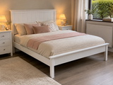 Bedroom with a white bed frame, pink bedding, and nightstands with lamps.