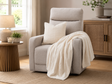 Beige upholstered recliner chair with padded arms, styled with a cream quilted throw and matching cushion, set in a warm cosy Irish living room with a side table, lamp, woven rug, and natural wood accents