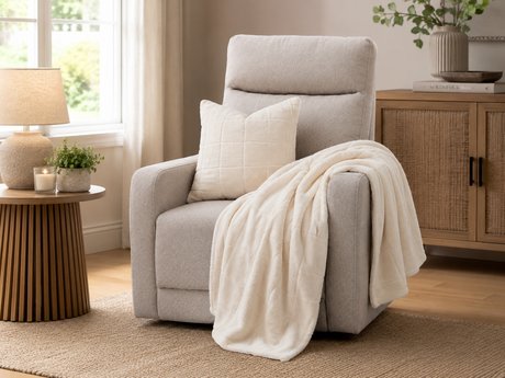 Beige upholstered recliner chair with padded arms, styled with a cream quilted throw and matching cushion, set in a warm cosy Irish living room with a side table, lamp, woven rug, and natural wood accents